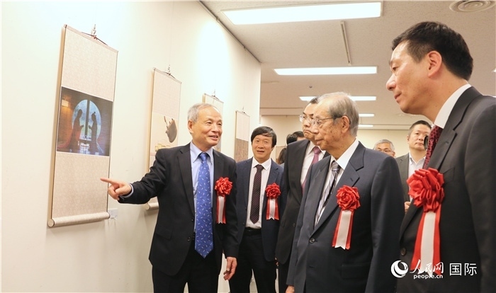 “湖州印象”攝影展主創(chuàng)、世界華人攝影協(xié)會副會長馮學(xué)敏向吳江浩大使、福田康夫前首相等嘉賓介紹展出作品。（人民網(wǎng) 許可攝）