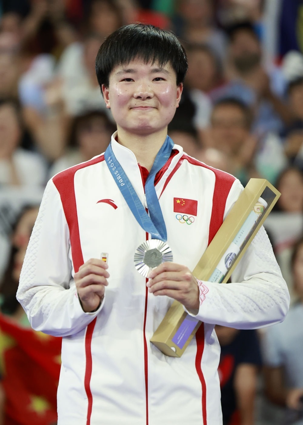 巴黎奧運(yùn)會(huì)羽毛球女子單打亞軍、中國選手何冰嬌在頒獎(jiǎng)儀式上一手握著銀牌，一手握著西班牙奧委會(huì)徽章（2024年8月5日攝）。新華社記者 任正來 攝